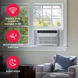Frigidaire 18,000 BTU Smart Window Room AC Model FHWW184WE2 installed in a white window, highlighting three key benefits: Wi-Fi connectivity for Alexa and Google Home, multi-direction airflow, and sleep mode. The room features a gray armchair and a dark brown side table.